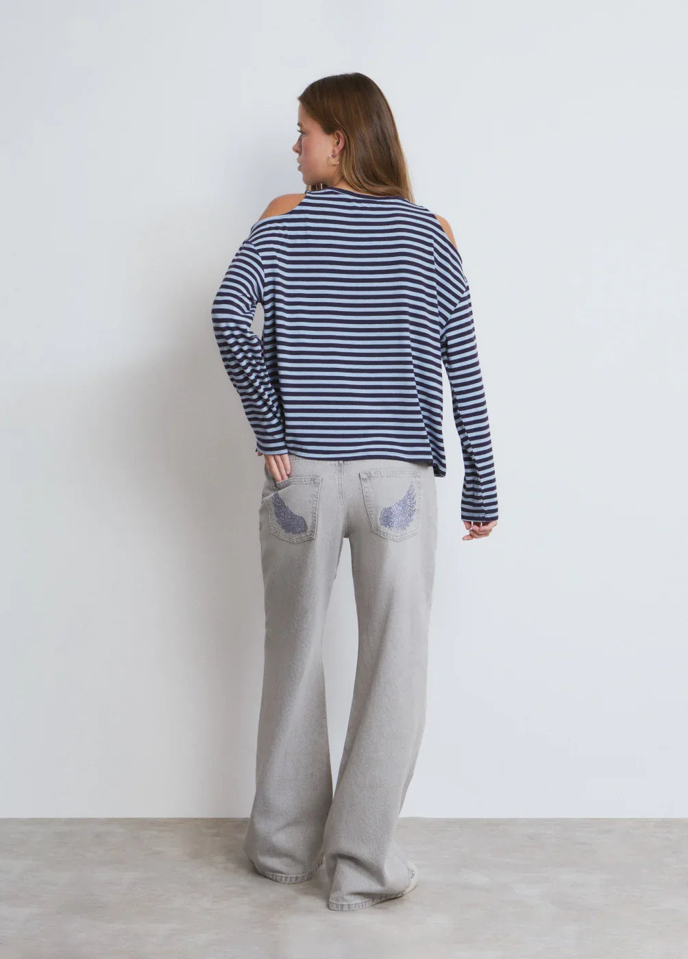 אישה עם חולצת פסים כחול-לבן ומכנסיים אפורים עם עיטורים על הכיסים, אופנת CHOZEN
