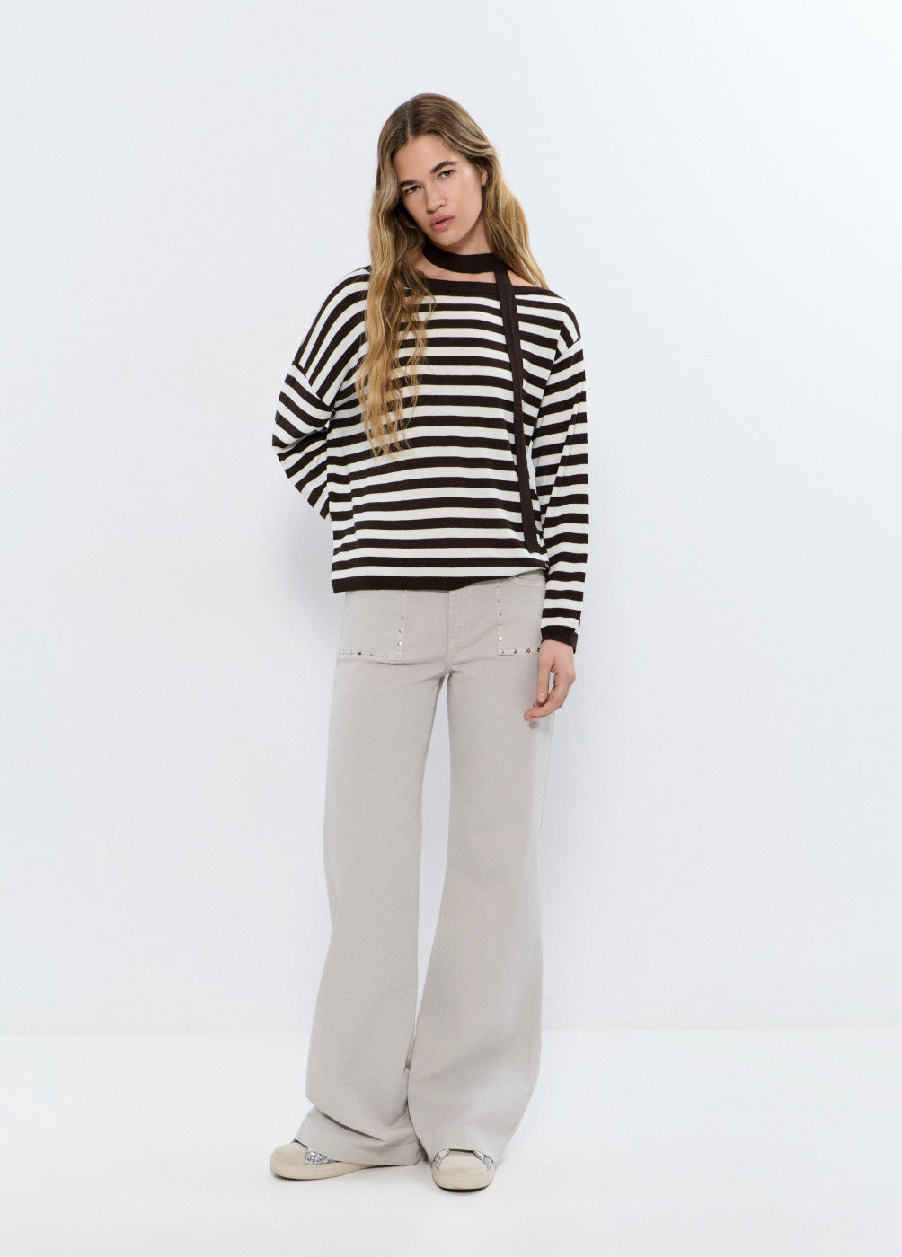 אישה לובשת סווטשרט פסים שחור לבן ומכנסיים בהירים בגזרה רחבה על רקע לבן