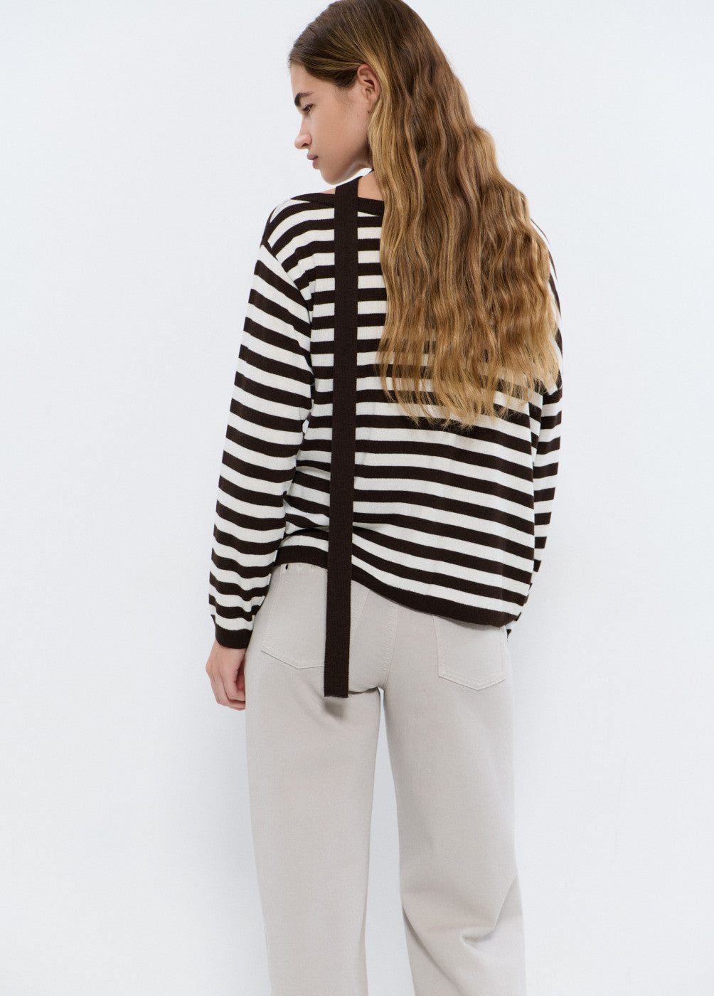 אישה עם שיער ארוך לובשת סוודר פסים שחור לבן ומכנסיים בהירים, מבט מאחור