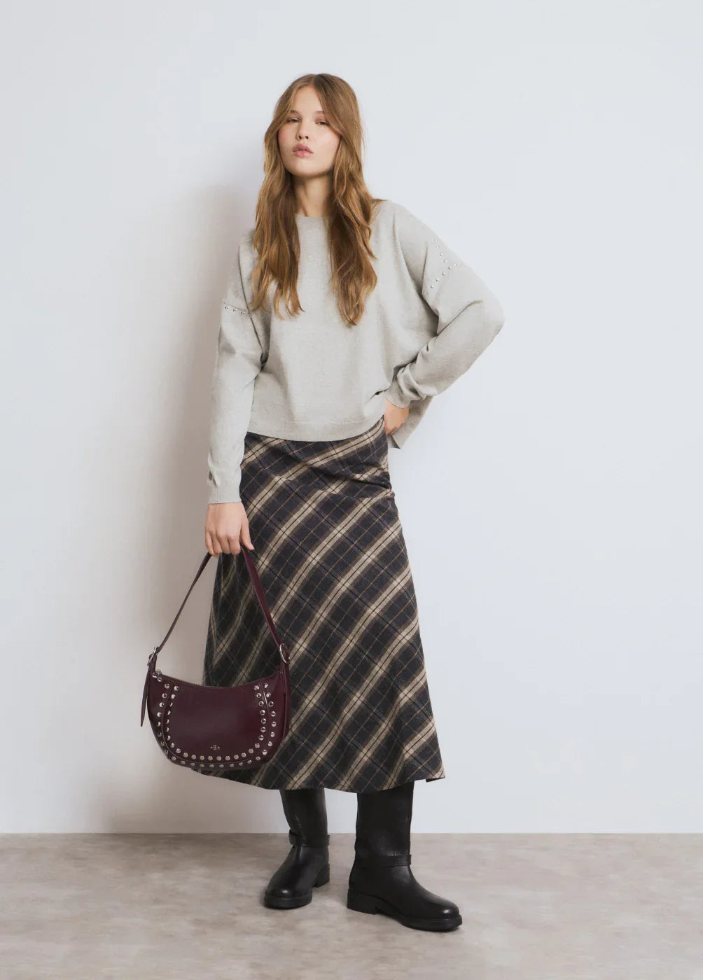 דגם אופנה בחצאית משובצת, חולצה אפורה, מגפיים שחורים ותיק בורדו, קולקציית CHOZEN