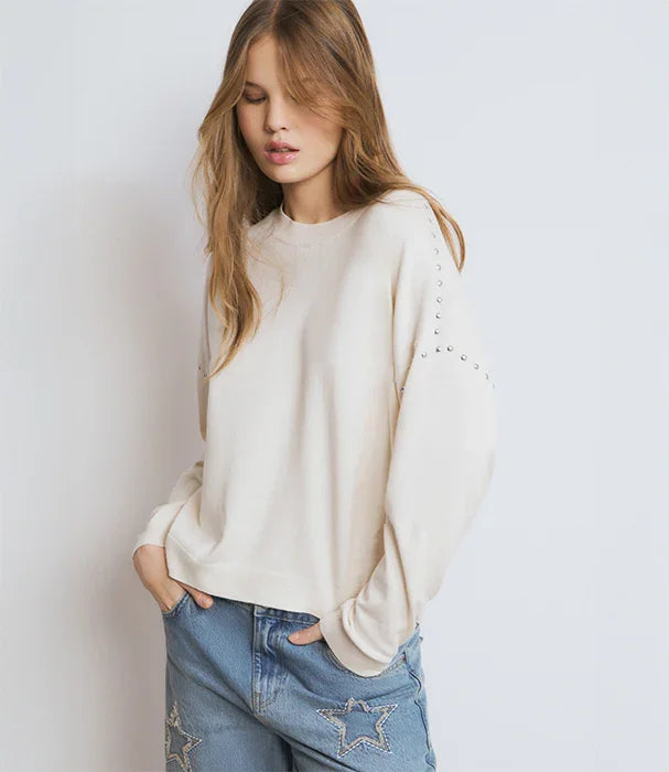 אישה לובשת סווטשירט שמנת עם ניטים בשרוולים וג'ינס כחול עם כוכבים, אופנה טרנדית CHOZEN