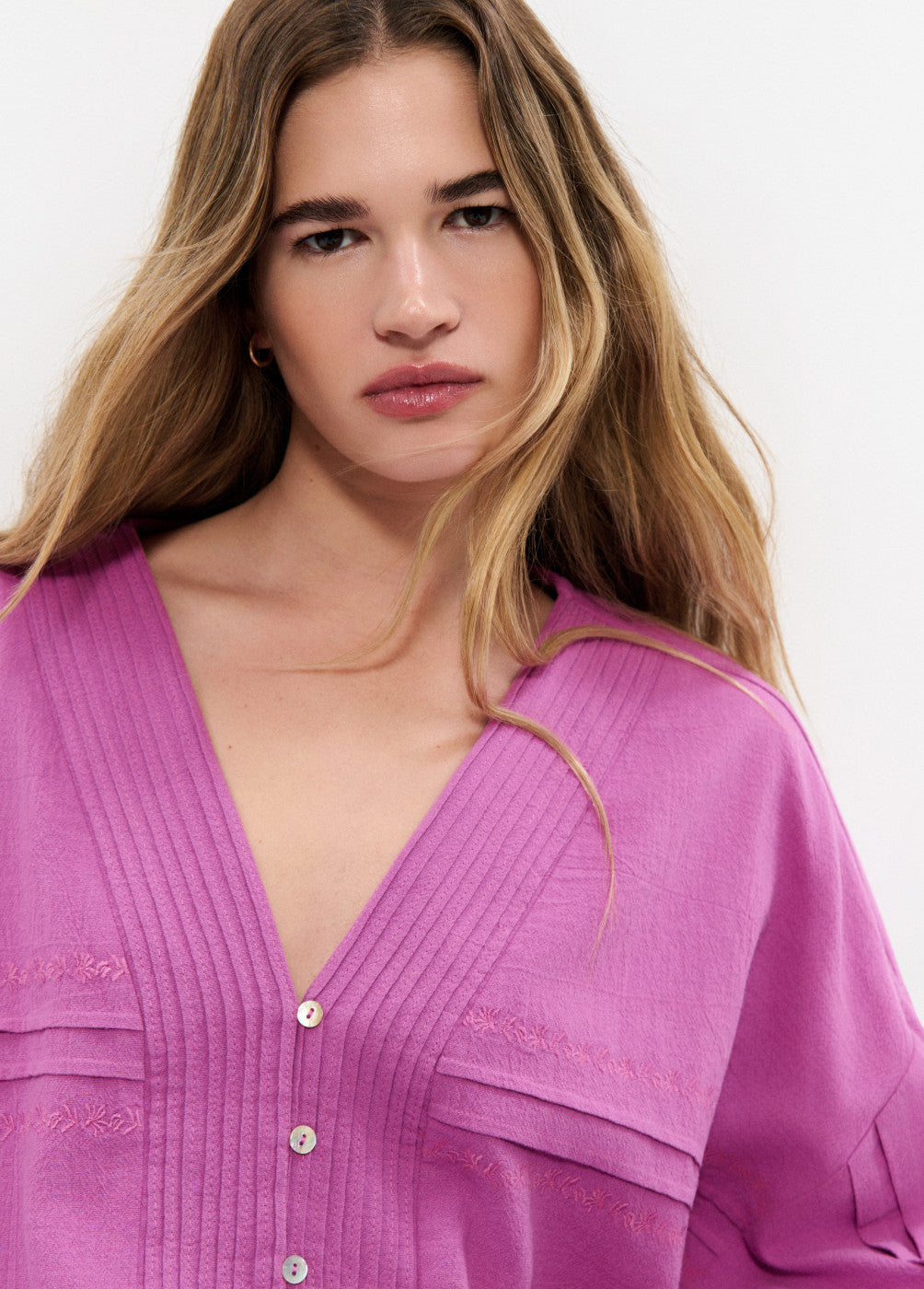 אישה עם חולצה סגולה מכופתרת, מפתח וי, רקמה עדינה, לצילום אופנה על רקע לבן