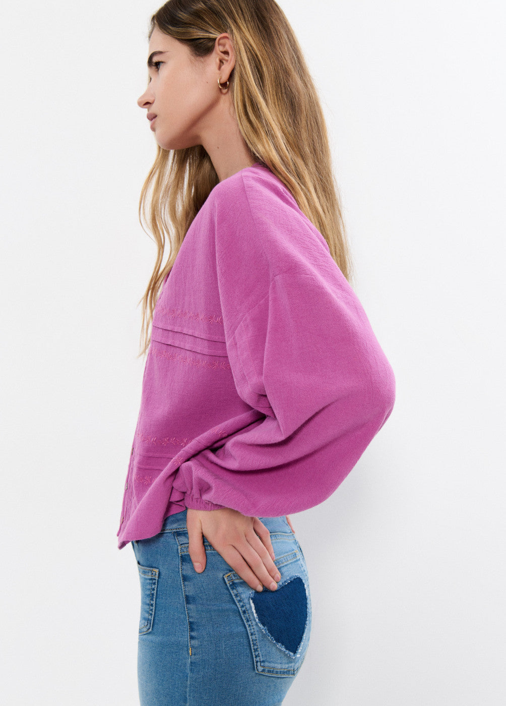 אישה עם חולצה ורודה רחבה ומכנס ג'ינס עם כיס לב בצבע כהה