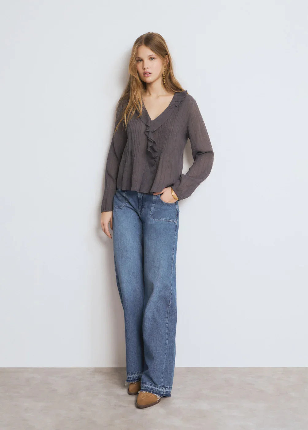אישה עומדת בלבוש אופנתי, חולצה כהה עם כפתורים ומכנסי ג׳ינס רחבים, צילום קטלוג CHOZEN