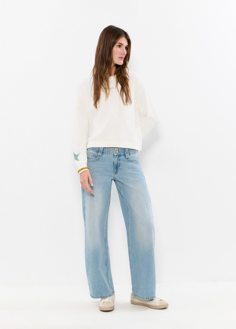 אישה עם סוודר לבן ומכנסי ג'ינס רחבים, לוק קז'ואל אופנתי על רקע לבן