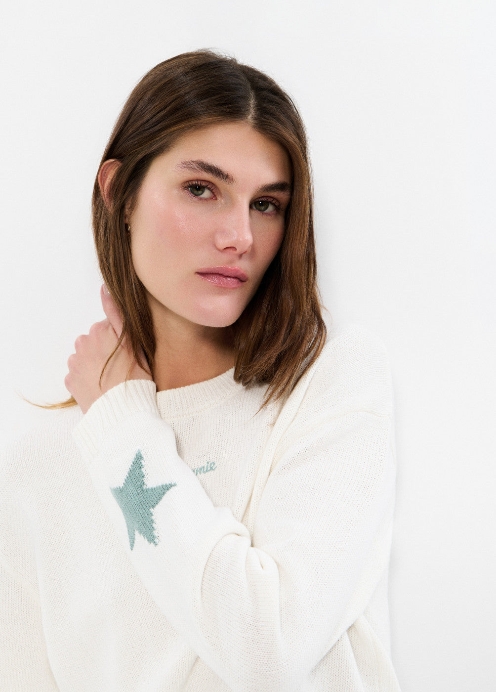 אישה עם סוודר לבן וכוכב ירוק על השרוול בצילום סטודיו אופנה
