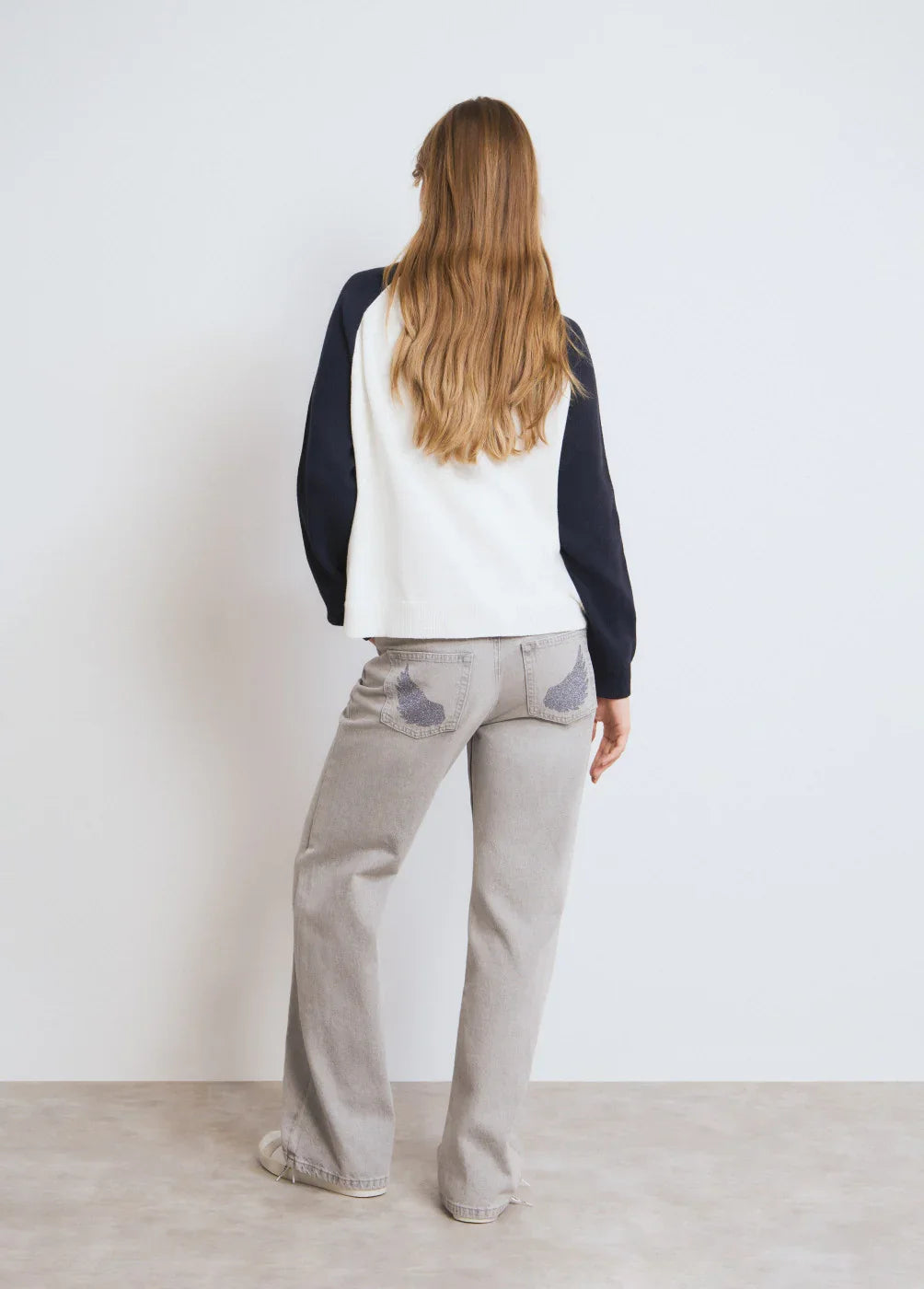 אישה עם שיער ארוך לובשת חולצה לבנה עם שרוולים כהים ומכנסי ג'ינס אפורים, צילום אחורי לקידום מותגי CHOZEN