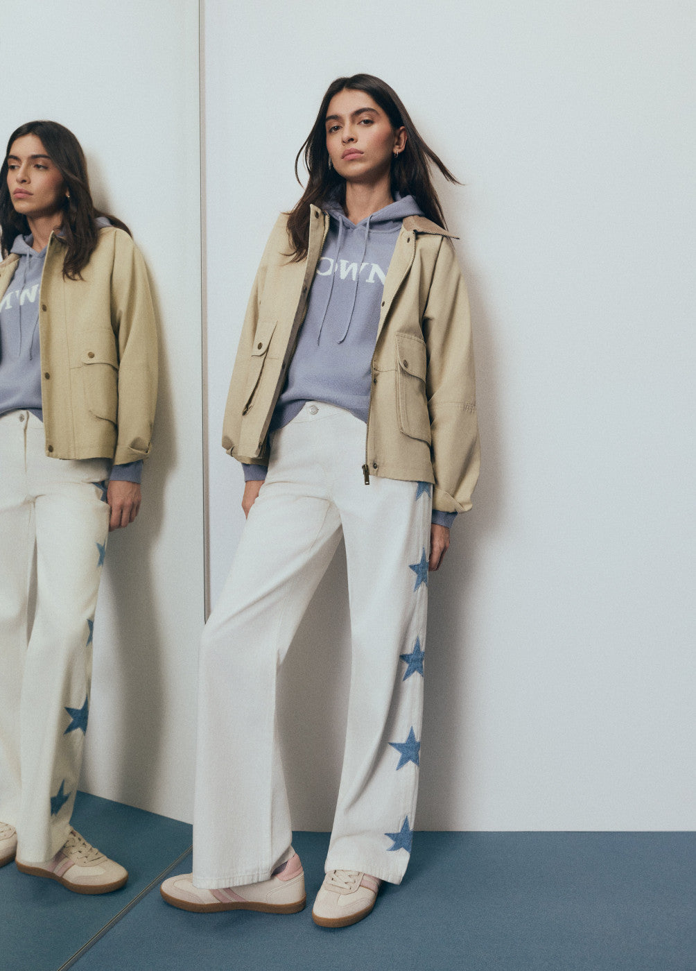 דוגמנית לובשת ז'קט בז' עם קפוצ'ון כחול ומכנסיים לבנים עם כוכבים כחולים בצד