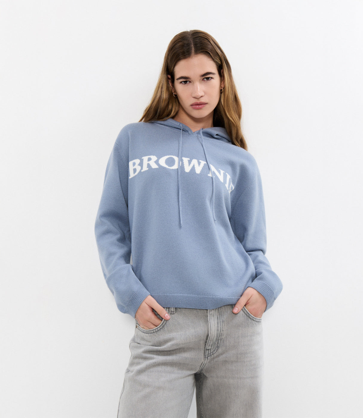 בחורה עם סווטשירט קפוצ'ון בצבע תכלת עם כיתוב BROWNIE ומכנסי ג'ינס אפורים