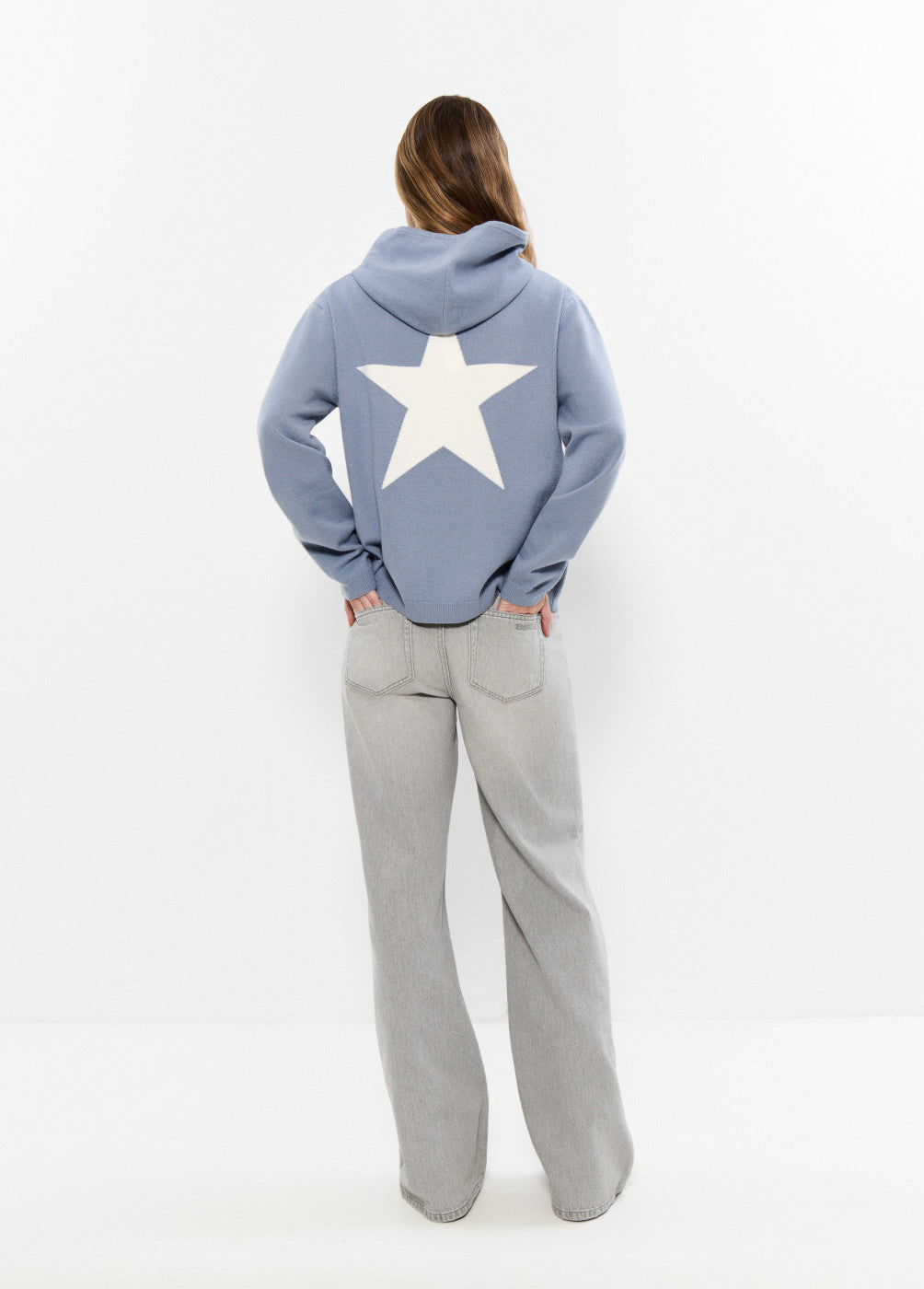 אישה עם קפוצ'ון כחול עם כוכב לבן בגב ומכנסי ג'ינס בהירים, אופנת נשים עדכנית