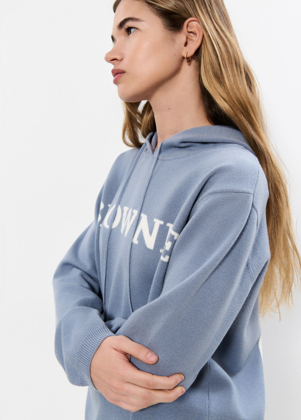 אישה עם סווטשירט קפוצ'ון כחול בהיר, כיתוב לבן, מראה אופנה יומיומי