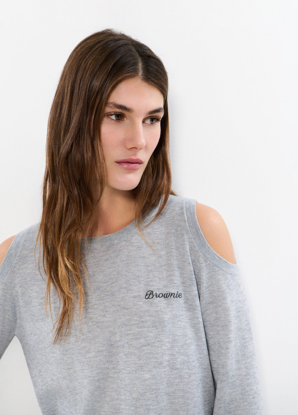 אישה לובשת חולצת סריג אפורה עם כתפיים חשופות וכיתוב Brownie רקום