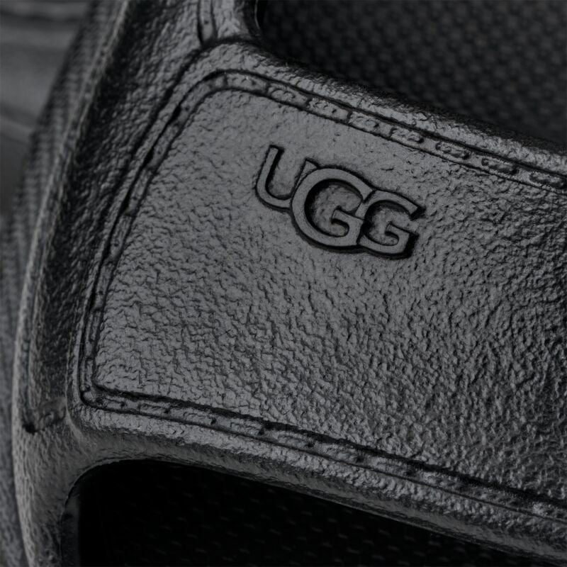 קלוז-אפ של סנדל עור שחור עם לוגו UGG מובלט, עיצוב יוניסקס אופנתי ואיכותי