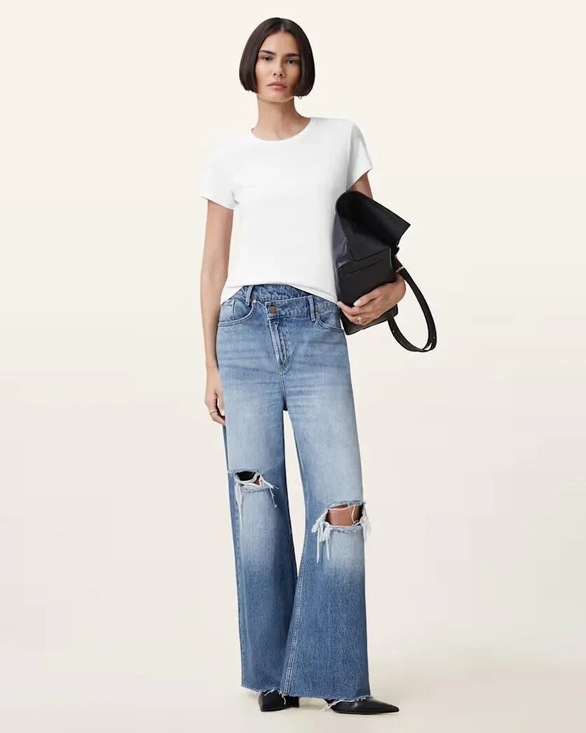 אישה לובשת ג'ינס רחב משופשף עם קרעים בברכיים וחולצת טי לבנה, מחזיקה תיק שחור