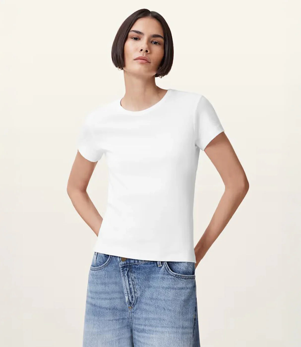 אישה לובשת חולצת טי שירט לבנה וג'ינס כחול, רקע בהיר, אופנת קיץ קז'ואל