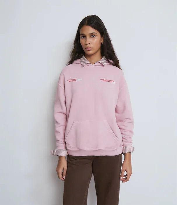 אישה לובשת סווטשירט ורוד עם כיתוב לבן, חולצה מתחת ומכנסיים חומים, מותג אופנה CHOZEN