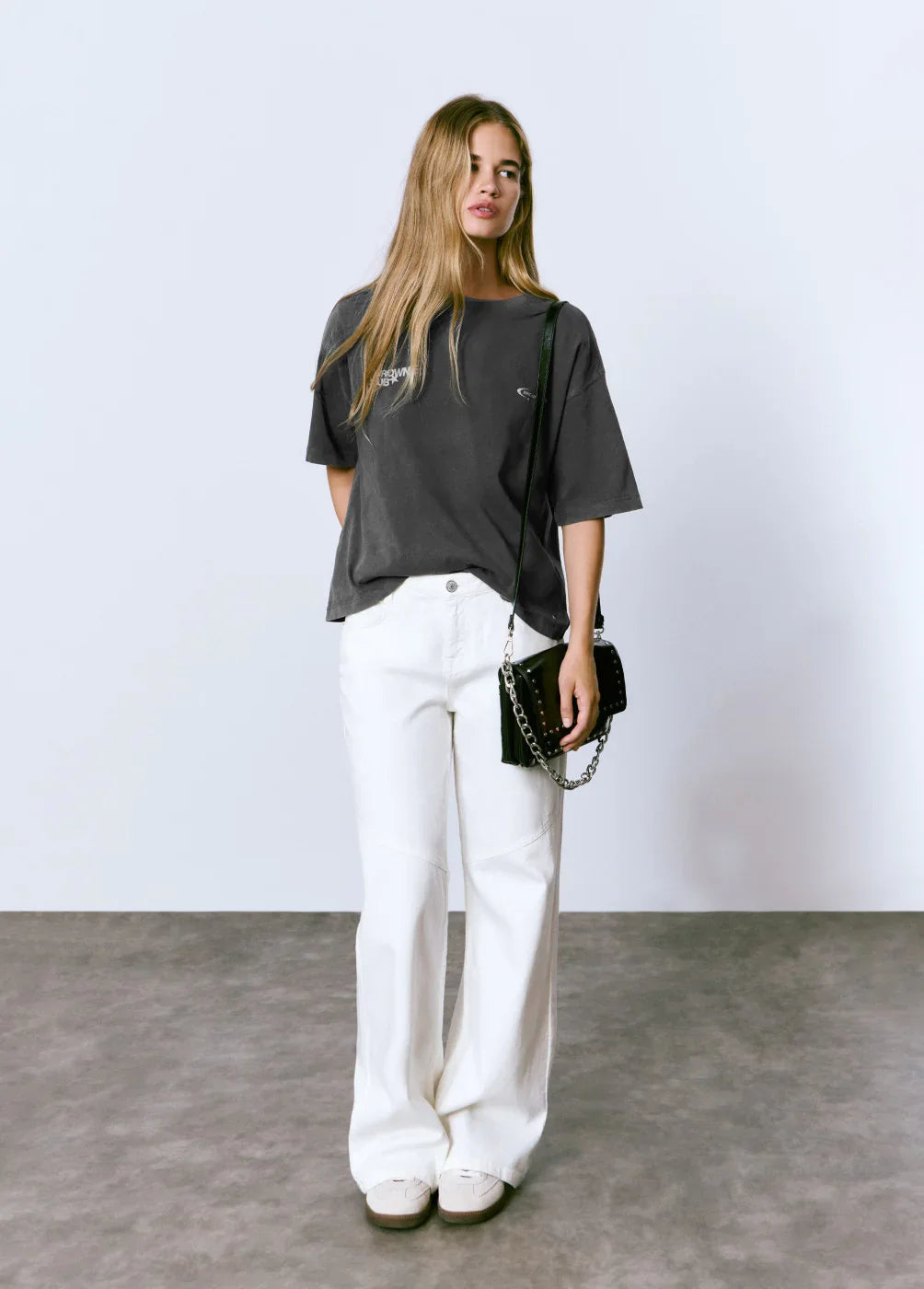 אישה לובשת חולצת טי שחורה, מכנסיים לבנים ותיק צד, צילום אופנה ל-CHOZEN