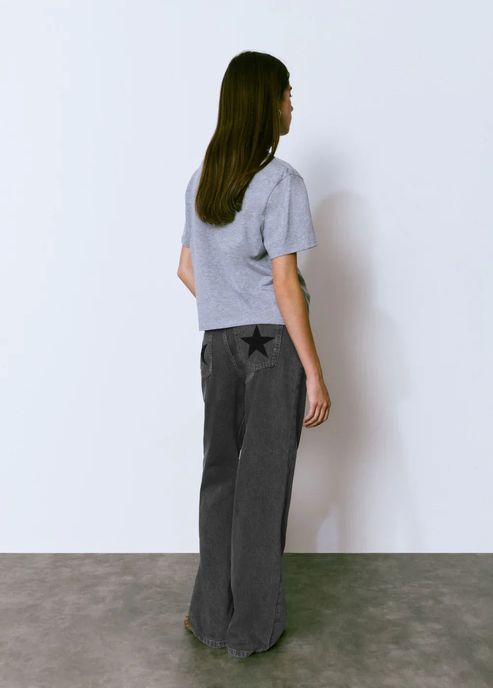 אישה עם חולצת טי אפורה ומכנסי ג'ינס שחורים עם כוכב שחור בכיס, אופנת CHOZEN