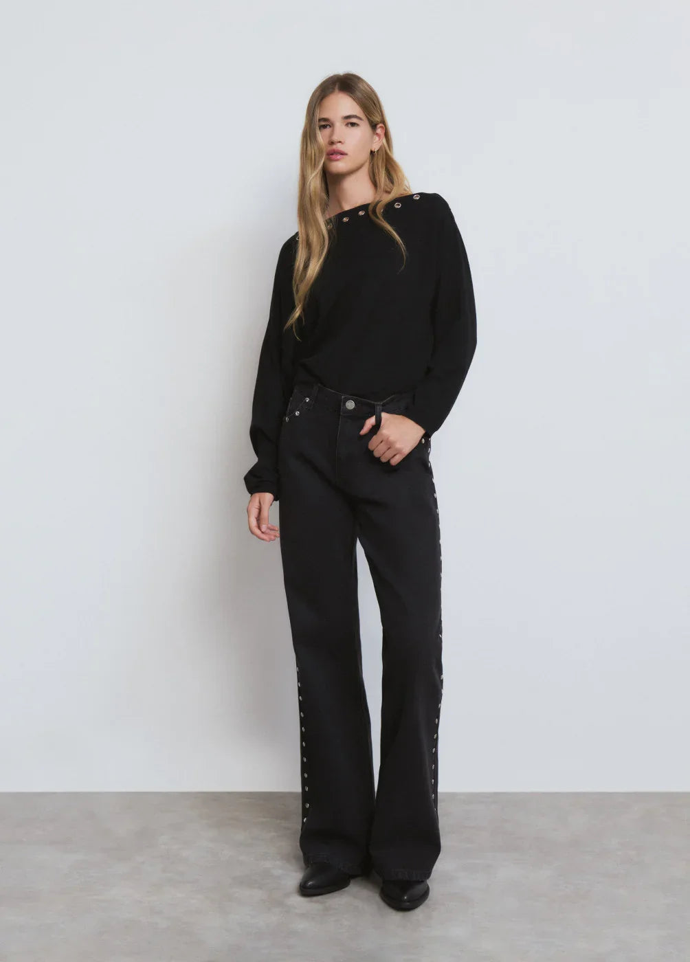 דוגמנית לובשת חולצה שחורה עם עיניות וכפתורים ומכנסיים שחורים, אופנה עדכנית ב-CHOZEN