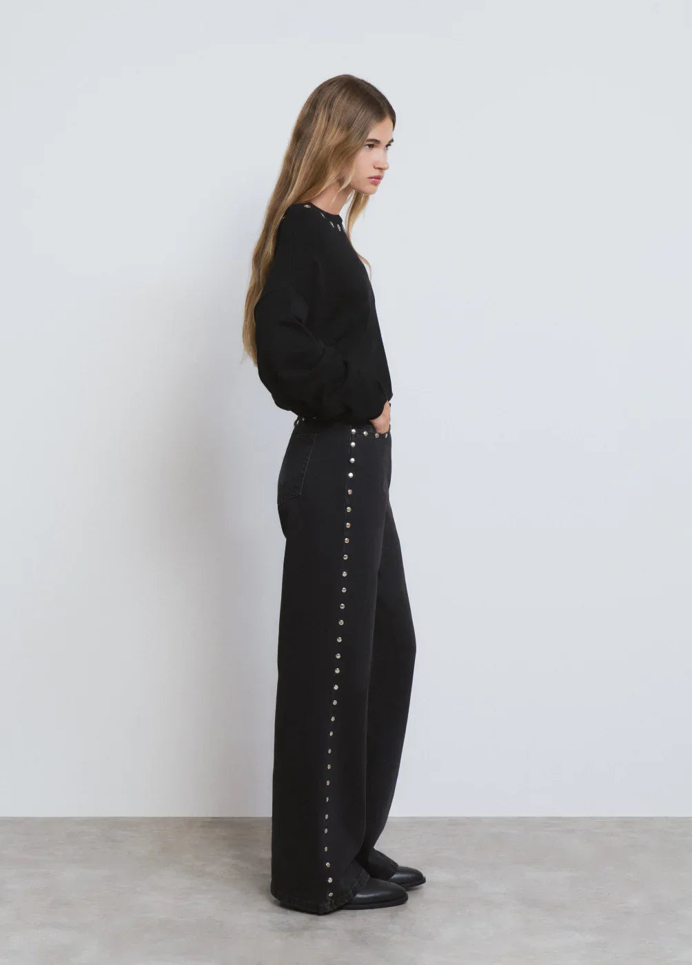 אישה עם חולצה שחורה ומכנסיים שחורים עם ניטים בצד, אופנת CHOZEN, צילום סטודיו