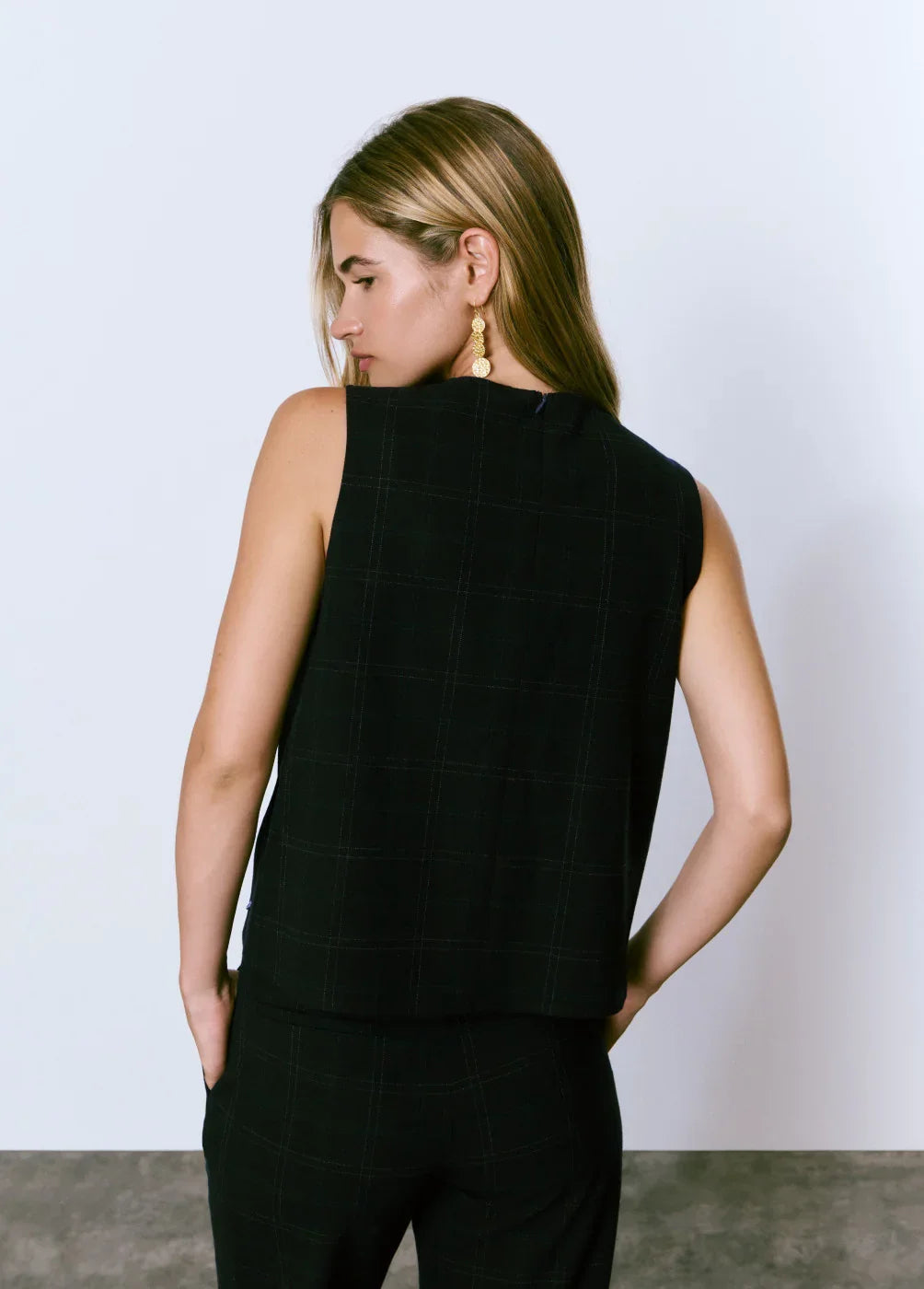 אישה עם שיער בלונדיני, עגילי זהב, לובשת חליפת שני חלקים שחורה מבית CHOZEN, מוצגת מהגב