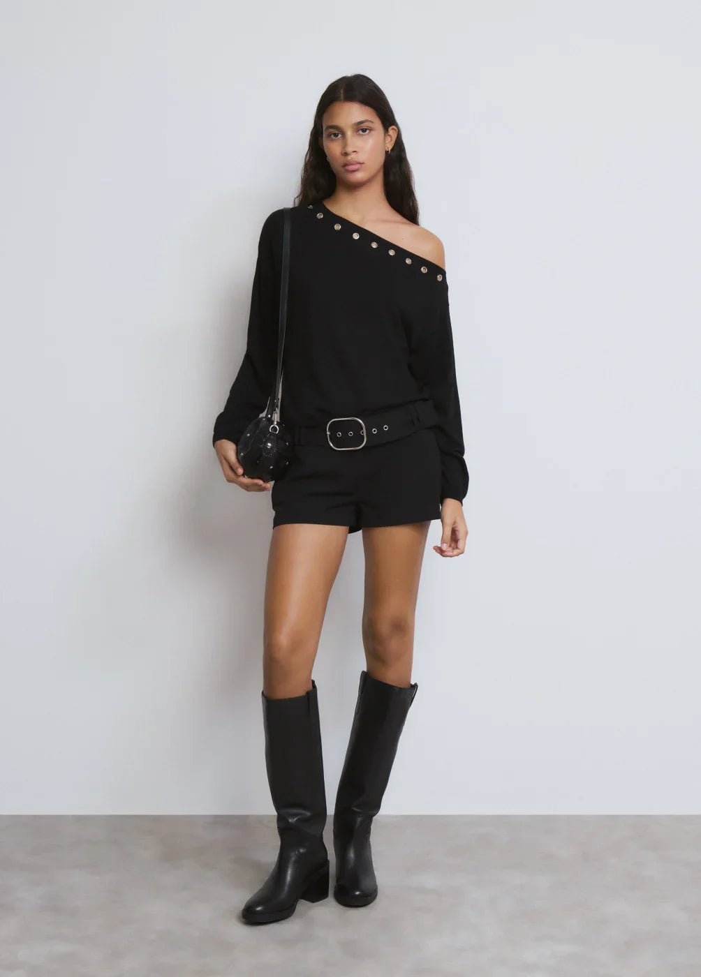 דוגמנית לובשת אוברול שחור קצר עם כתף חשופה, מגפיים וחגורה, CHOZEN מותגים מובילים