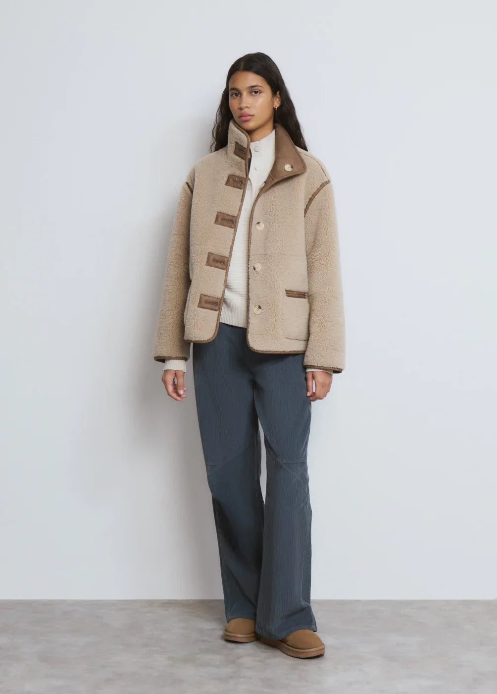 אישה לובשת ג'קט טדי בז' אופנתי של CHOZEN מקבוצת אלפא, מכנסיים כהים ונעלים חומות