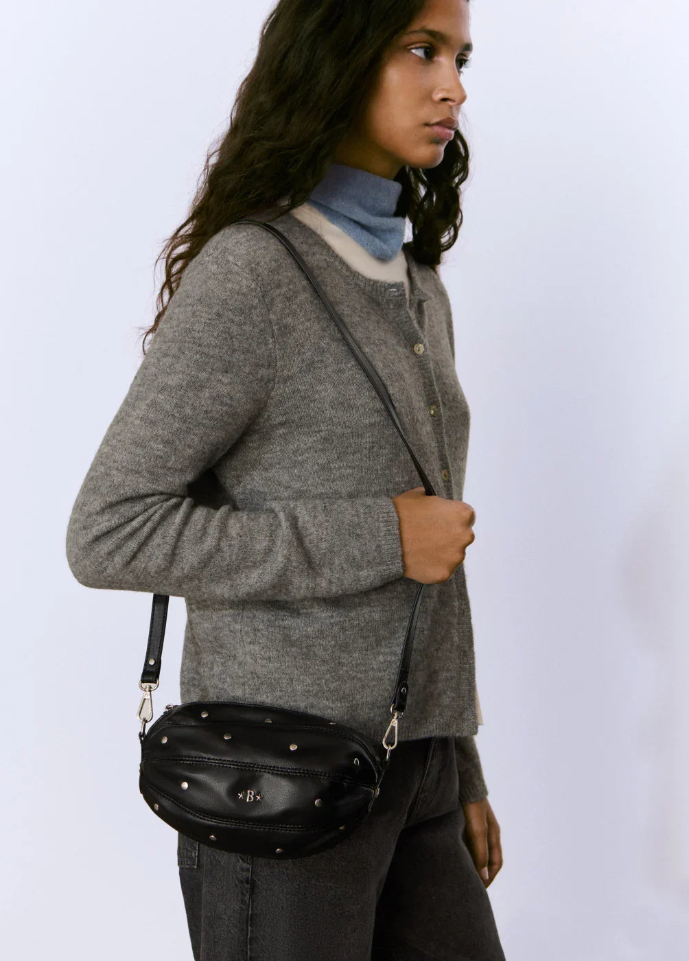 אישה עם תיק צד שחור מעוצב עם ניטים, לבושה בסוודר אפור, אופנה מודרנית CHOZEN