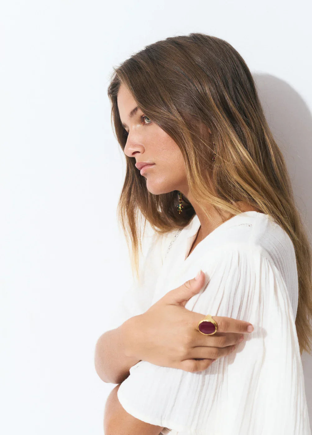 אישה עם שיער חום ארוך לובשת בגדים לבנים, עונדת טבעת זהב עם אבן אדומה, צילום סטודיו CHOZEN