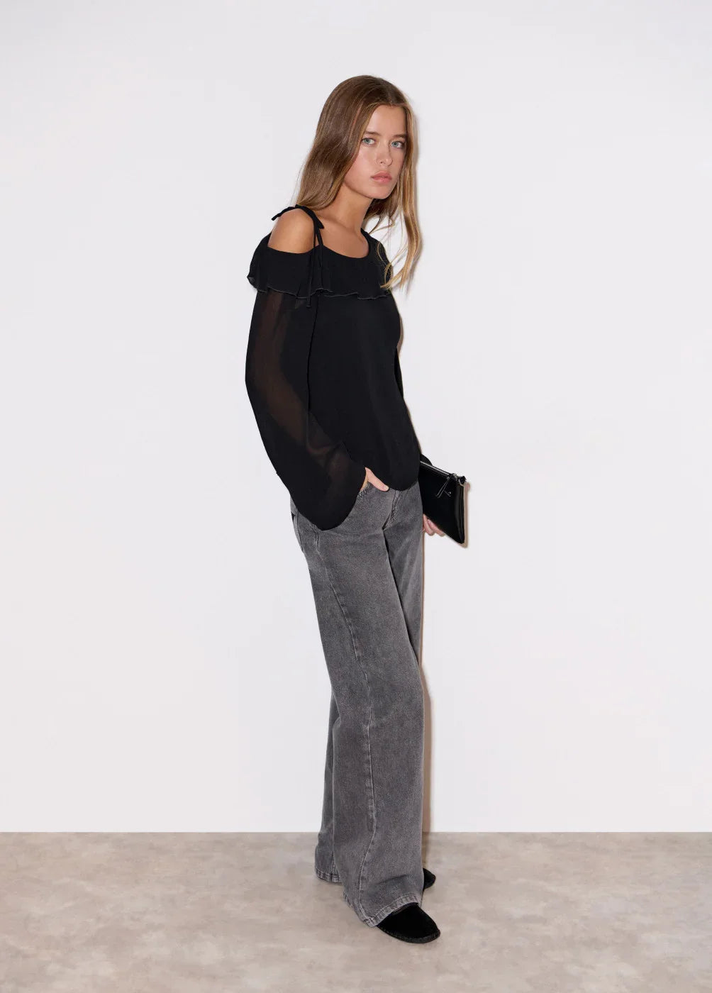 אופנה לנשים CHOZEN, דוגמנית לובשת חולצה שחורה עם כתפיים חשופות ומכנסי ג'ינס אפורים