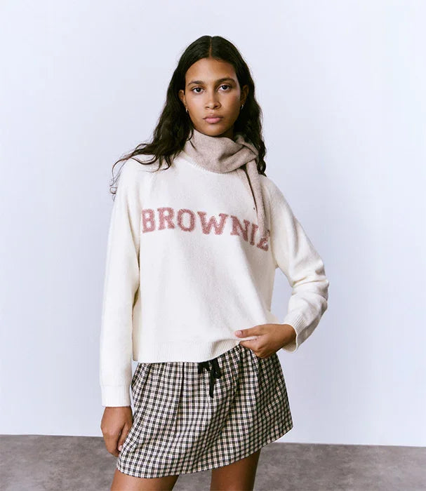 דוגמנית לובשת סוודר קרם עם הכיתוב BROWNIE וחצאית משובצת, אופנת נשים CHOZEN