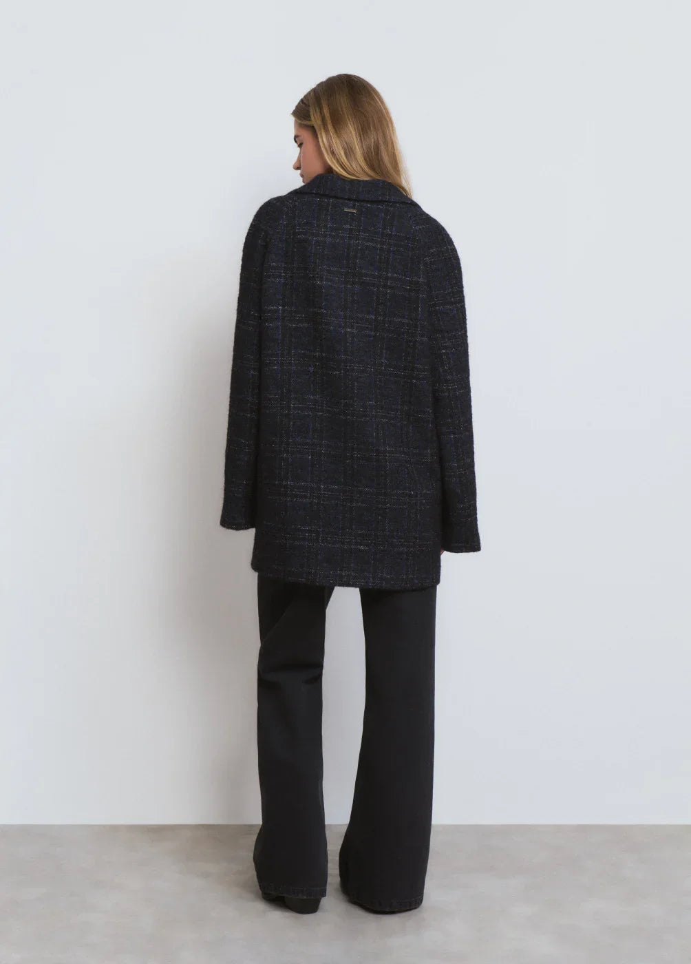 אישה עם שיער בלונדיני לובשת מעיל שחור מבד משובץ ומכנסיים שחורים, צילום גב, CHOZEN