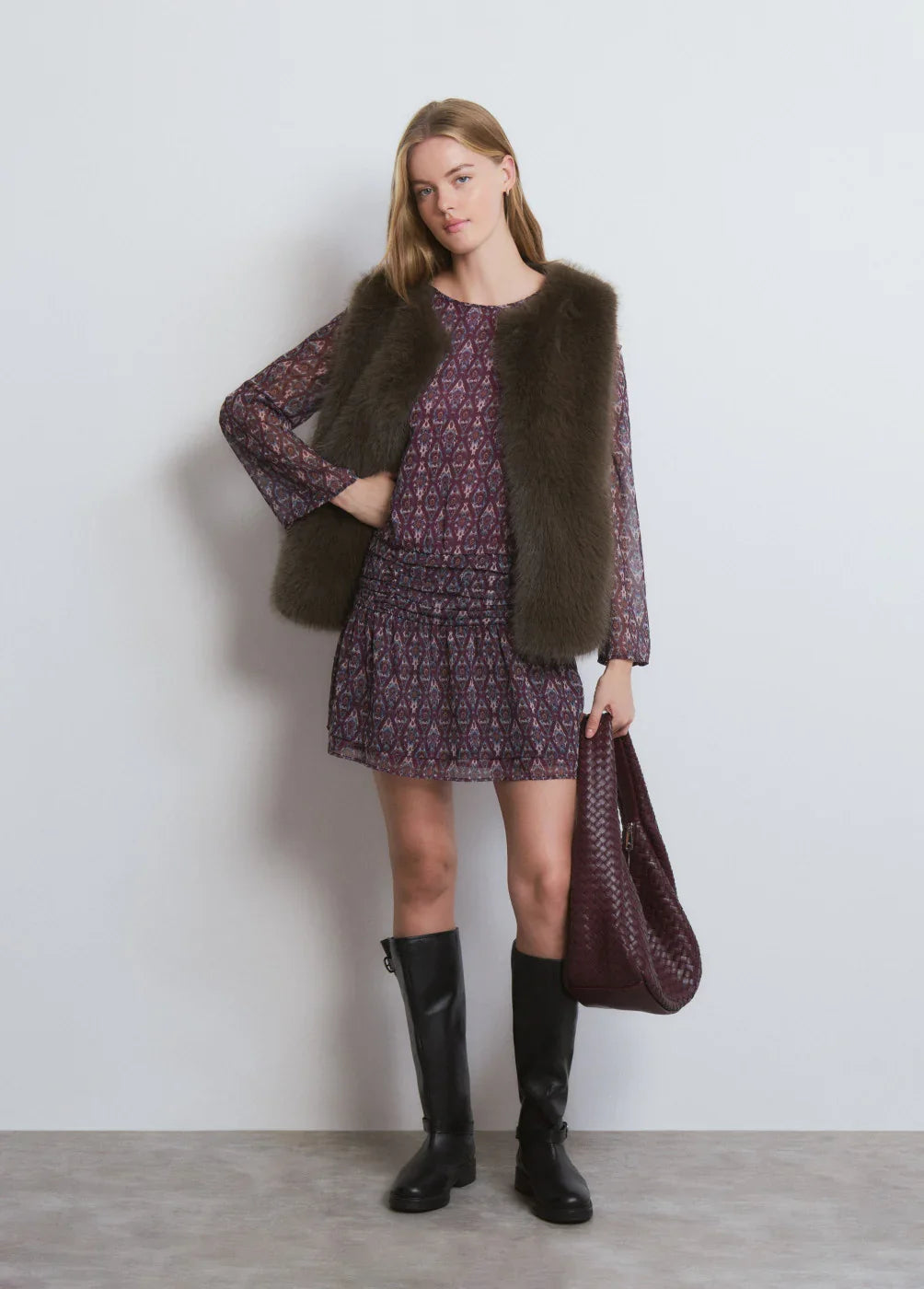 דוגמנית לובשת שמלת הדפס סגולה, וסט פרווה חום, מגפיים שחורים, ותיק סרוג, CHOZEN אופנה