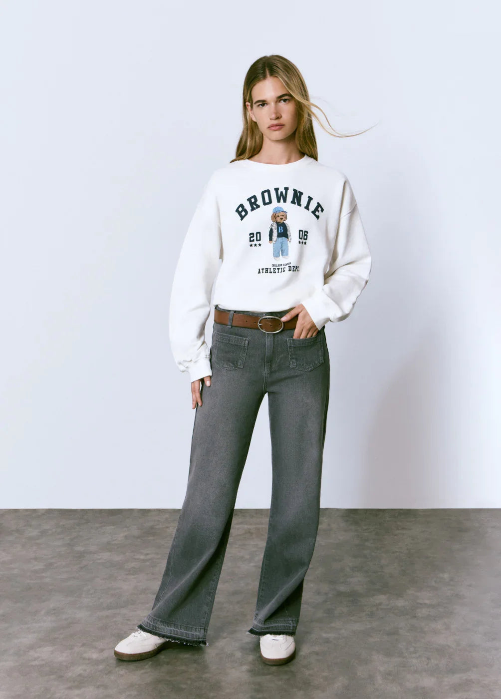 אישה לובשת סווטשירט לבן עם דובי ומכנסי ג'ינס אפורים, אופנת CHOZEN קז'ואל לנשים