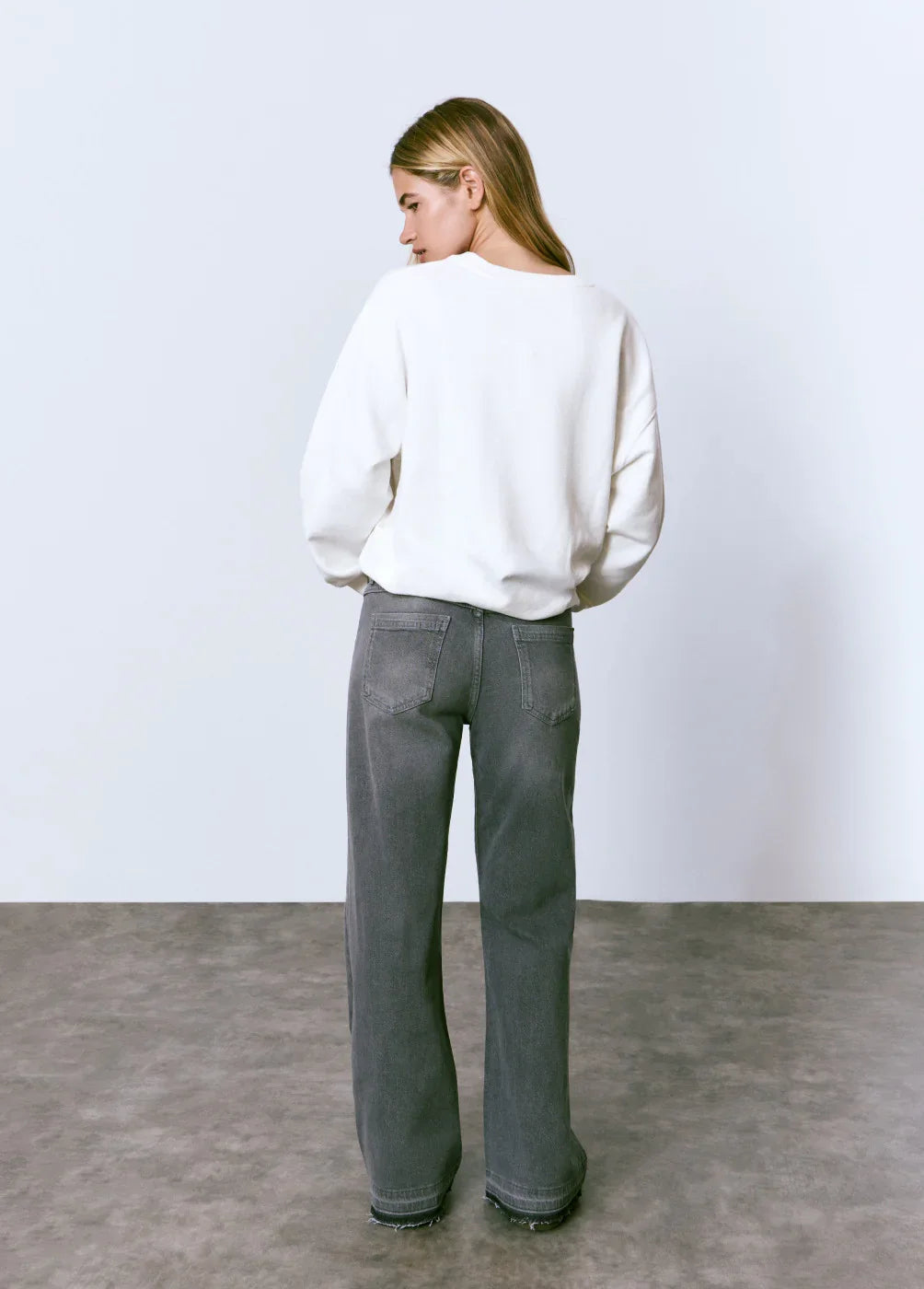 אישה עם שיער בלונדיני לובשת סווטשירט לבן וג'ינס רחב אפור, אופנת CHOZEN