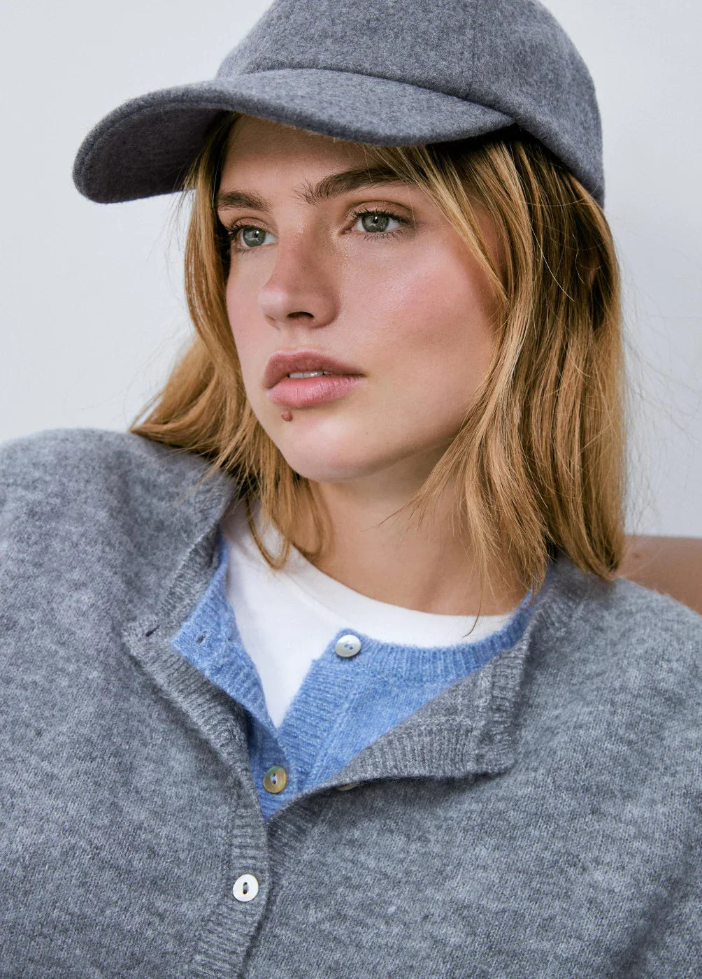 אישה בכובע אפור, סוודר אפור וכפתורים, אופנה עדכנית CHOZEN, קבוצת אלפא