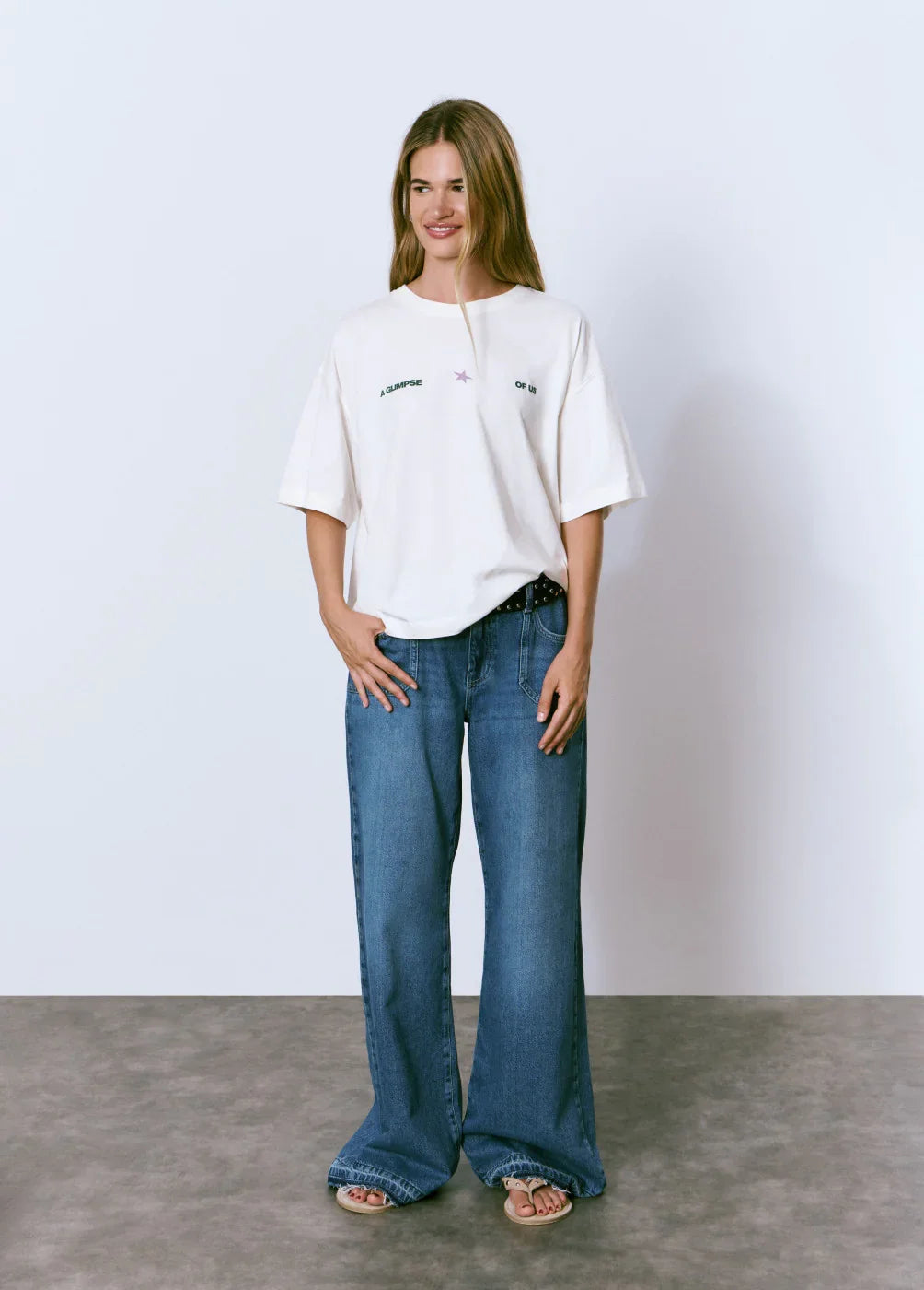 אישה לובשת חולצת טי שרט לבנה עם כיתוב A GLIMPSE OF US וג'ינס כחול רחב, אופנה CHOZEN
