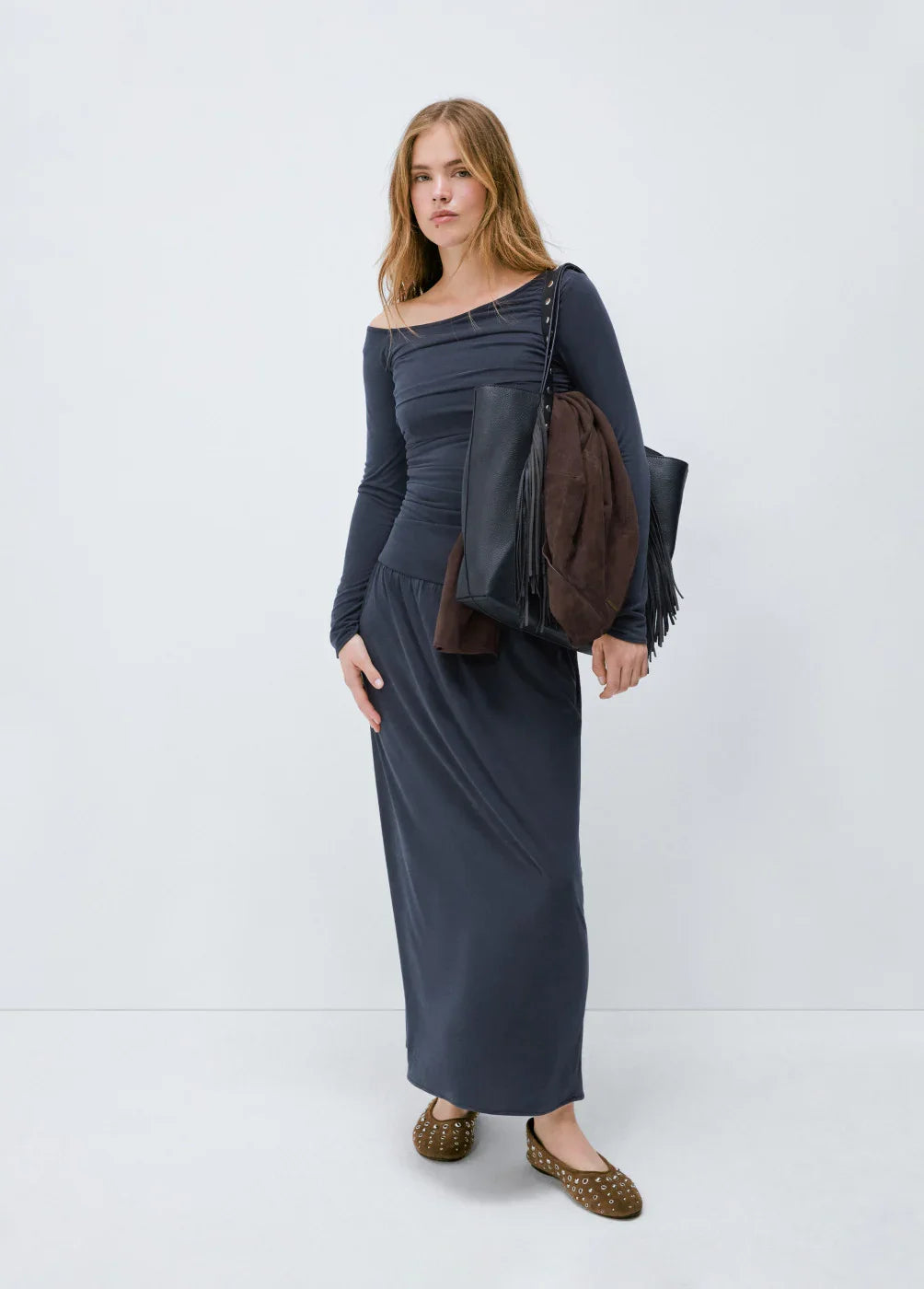 אישה לובשת שמלת מקסי כחולה עם שרוולים ארוכים, תיק שחור ומעיל חום, אופנת CHOZEN