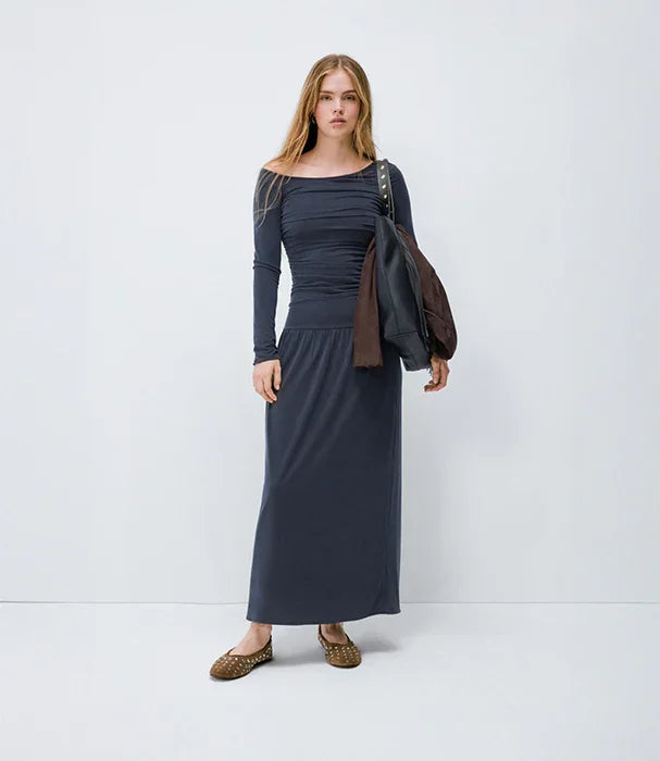 דגם אופנה של CHOZEN בשמלת מקסי כחולה, נעלי שטוח, ז'קט על הכתף, רקע לבן