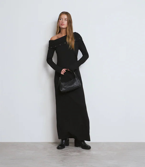 אישה לובשת שמלת ערב שחורה ארוכה עם כתף אחת, מחזיקה תיק יד שחור, אופנה יוקרתית CHOZEN