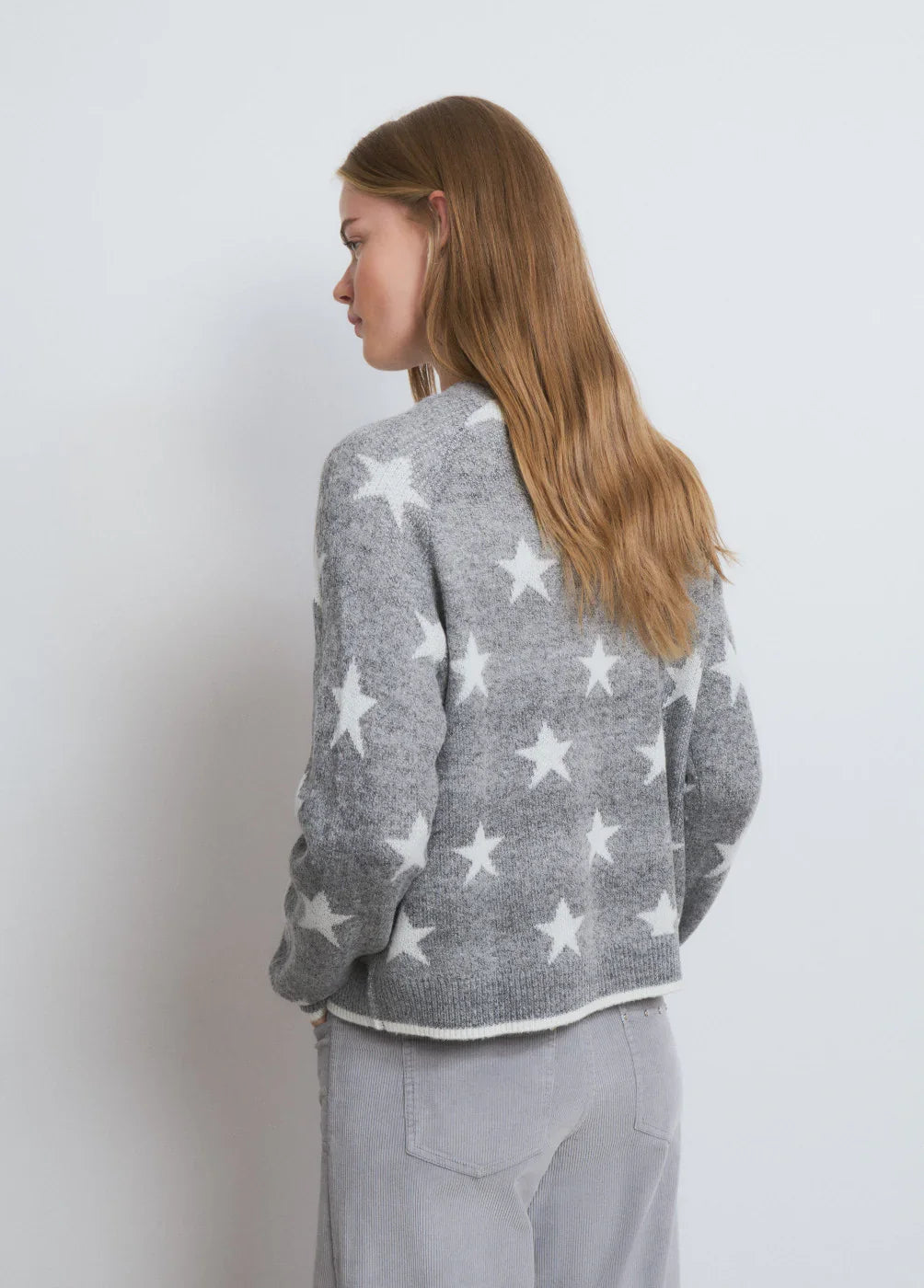 אישה לובשת סוודר אפור עם כוכבים לבנים מבית CHOZEN, צילום אופנה נגד קיר לבן