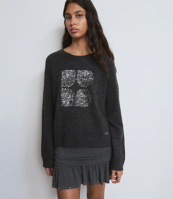 דוגמנית לובשת סוודר שחור של CHOZEN עם הדפס נצנצים, על רקע קיר לבן