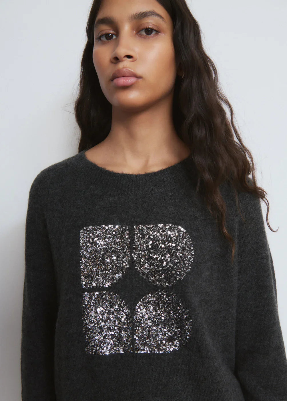 דוגמנית לובשת סוודר אפור עם פאייטים כסופים בצורת לוגו, אופנה טרנדית CHOZEN