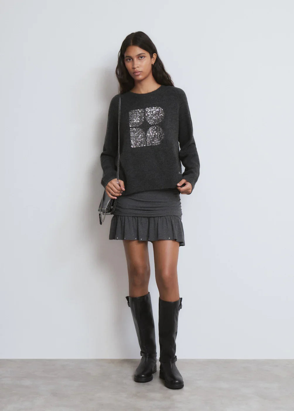 אישה לובשת סוודר אפור עם פאייטים וחצאית קצרה אפורה, מגפיים שחורים, אופנה לנשים CHOZEN