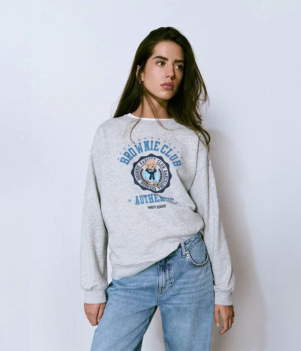 אישה לובשת סווטשירט אפור עם הדפס Brownie Club ומכנסי ג'ינס, אופנת נשים ב-CHOZEN
