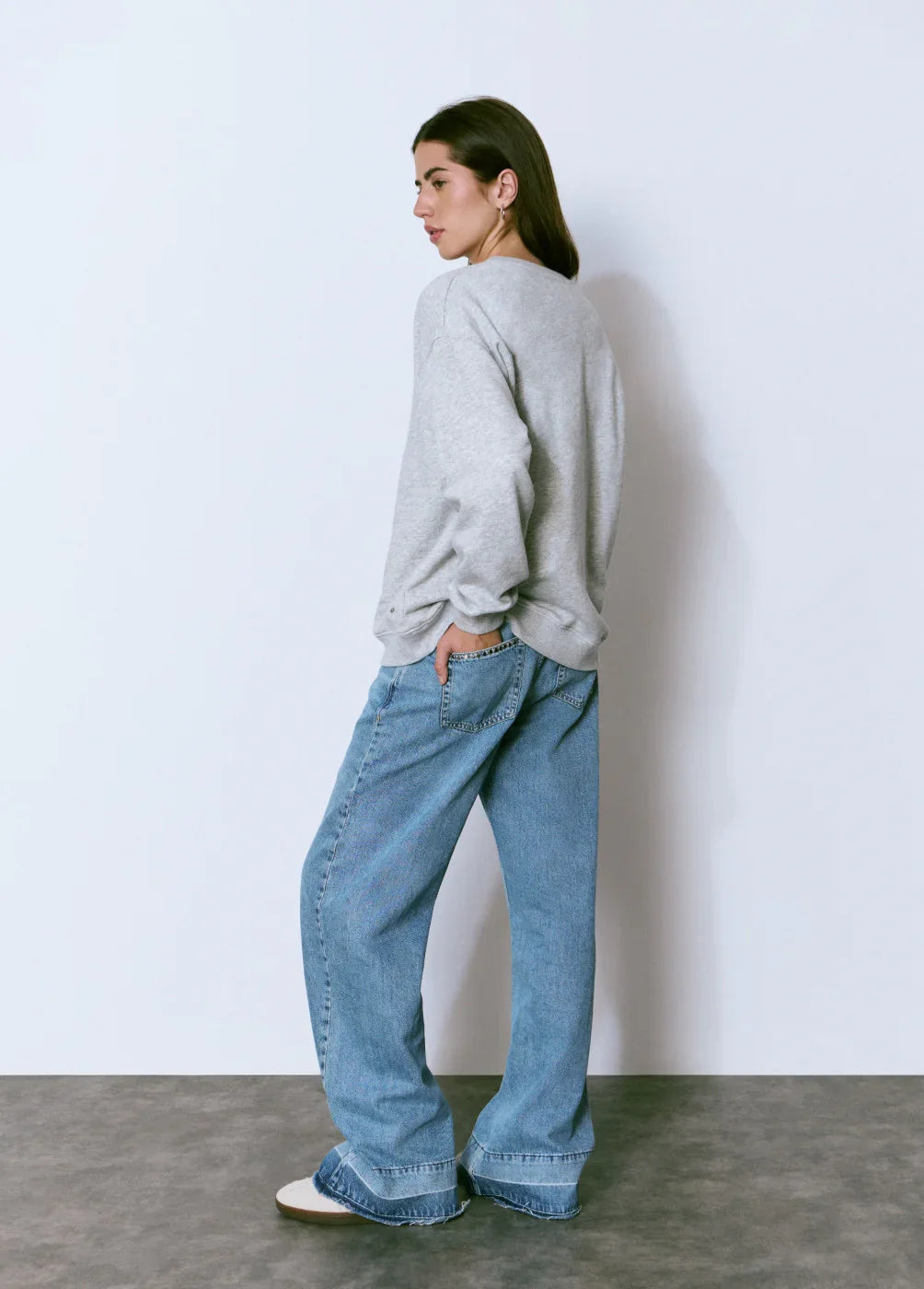 דוגמנית עם סווטשירט אפור ומכנסי ג'ינס בגזרה רחבה, אופנת CHOZEN, רקע לבן