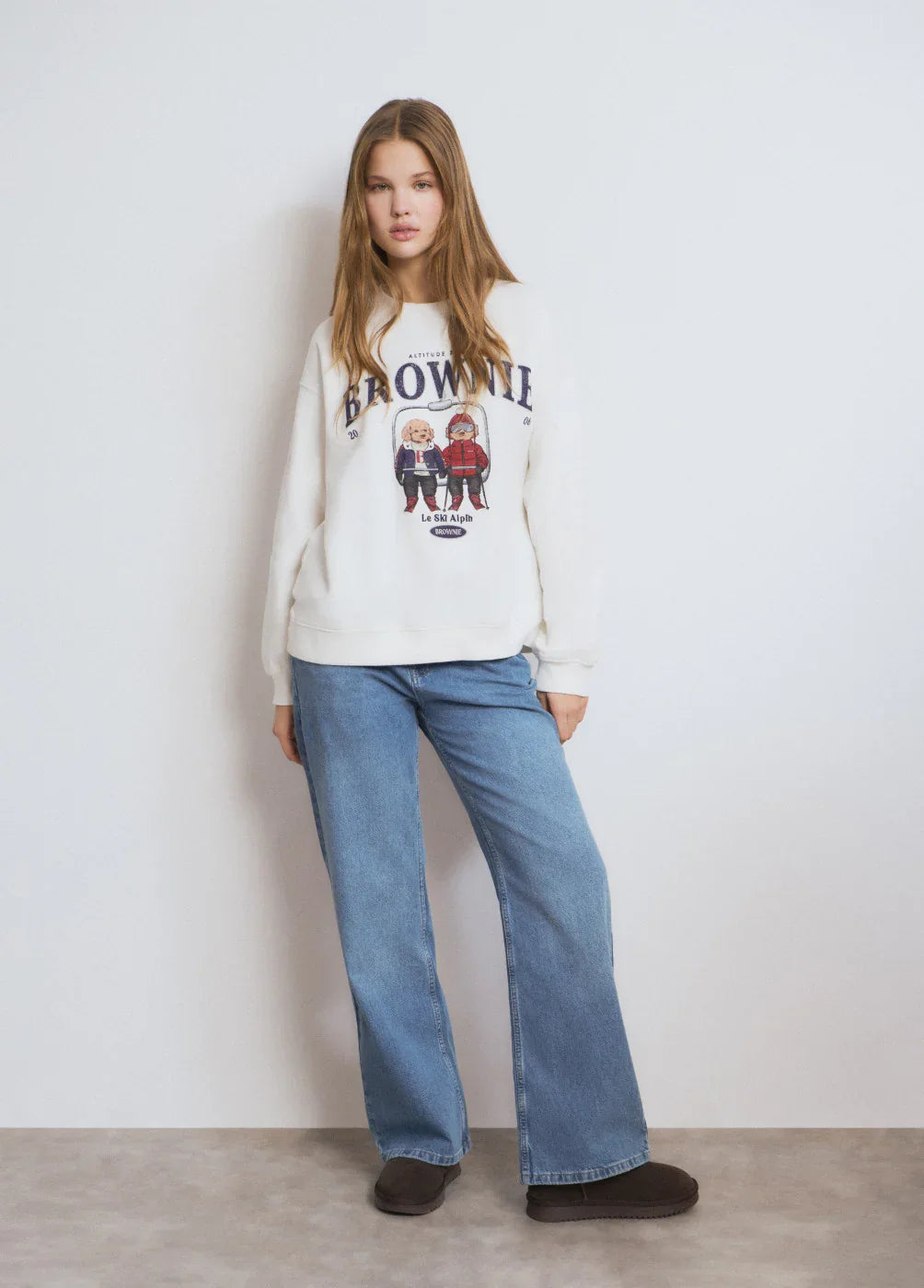 דוגמנית לובשת סווטשרט BROWNIE לבן עם הדפס דמויות, ג'ינס רחב ונעליים כהות, קולקציית CHOZEN