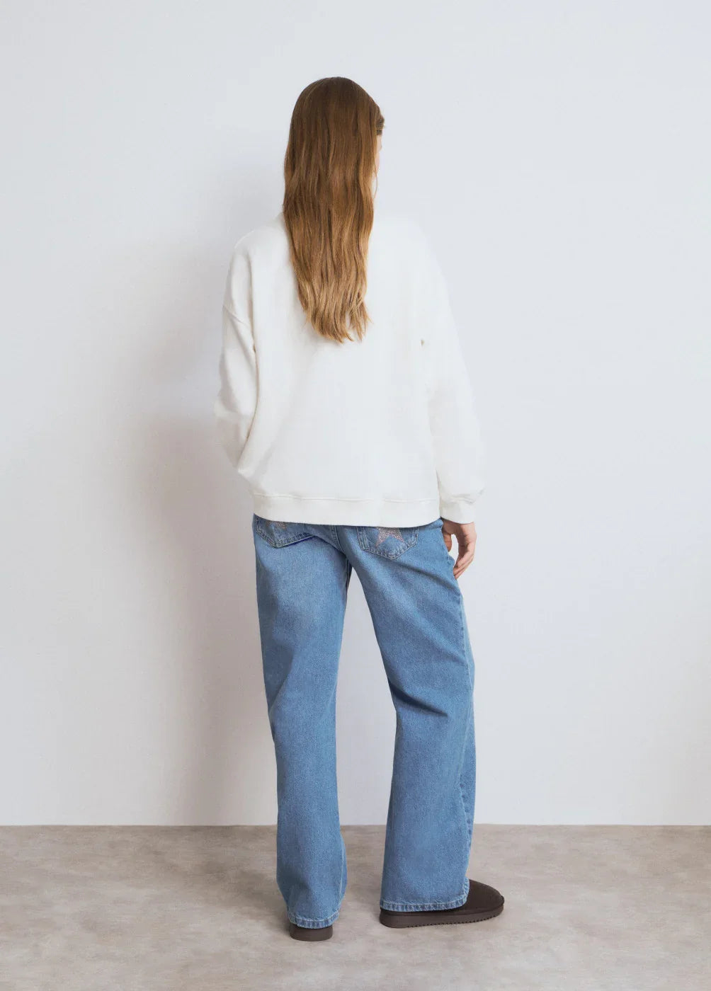 אישה עם שיער ארוך לובשת ג'ינס כחול רחב וסווטשירט לבן, מצולמת מהגב, CHOZEN אופנה