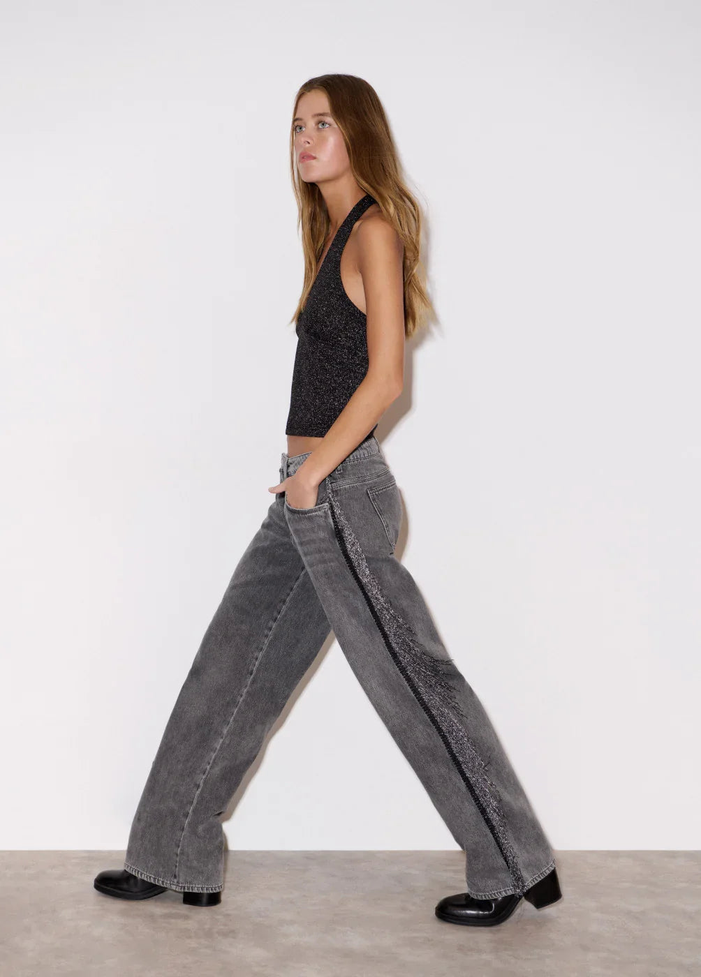 אישה מדגמנת ג'ינס אפור רחב עם פס דקורטיבי וכ топ נצנצים שחור, צ'וזן אופנה