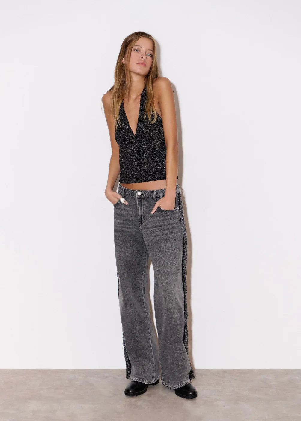 דוגמנית לובשת גופיה שחורה נוצצת ומכנסי ג'ינס רחבים בגוון אפור מבית CHOZEN